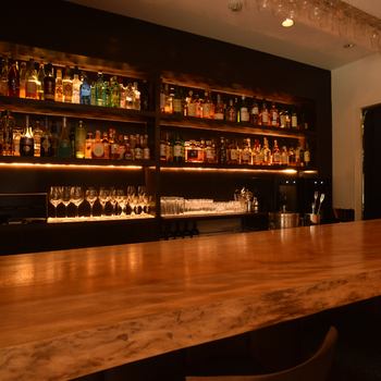 在吧台享用轻松的饮品，吧台设有一个后吧吧台，里面摆放着各种酒瓶、平静的灯光和钢琴爵士 BGM。