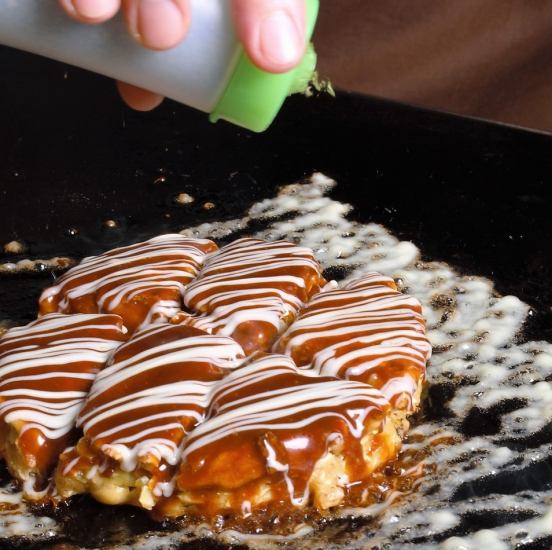 Okonomiyaki baked on an iron plate is appetizing with the aroma of the sauce