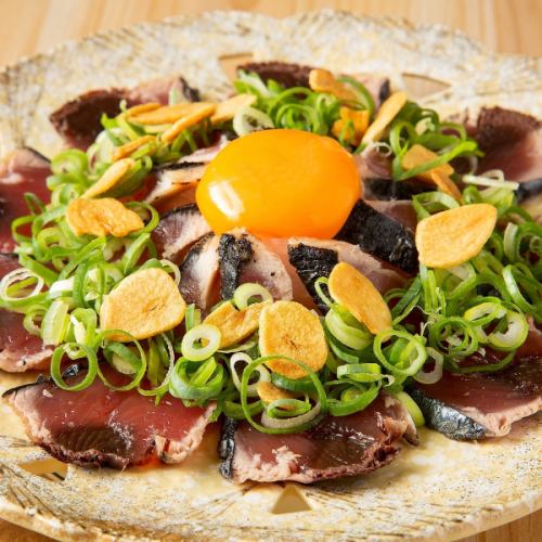 Seared bonito covered in green onions and topped with egg yolk