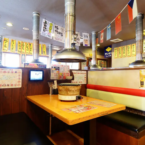 ゆったりと座れるベンチシートが特徴のテーブル席は、長時間の食事や宴会利用でも疲れにくく、リラックスして過ごすことができます。頭上には排気ダクトが設置され、焼肉特有の煙や匂いをしっかり吸引。壁一面に貼られたメニュー短冊やポップが、活気ある焼肉店ならではの雰囲気を高め、食欲を一層引き立ててくれます。