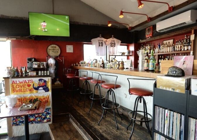 野球とバスケ好きが集まる、浦添市伊祖のスポーツバー『ROSSO』。非公認ながら熱いヤクルトスワローズファンが集い、琉球ゴールデンキングス公認の応援店として、迫力ある試合を大型モニターで楽しめます。世界各国のビールやクラフトビールを片手に、熱い夜を過ごしませんか？