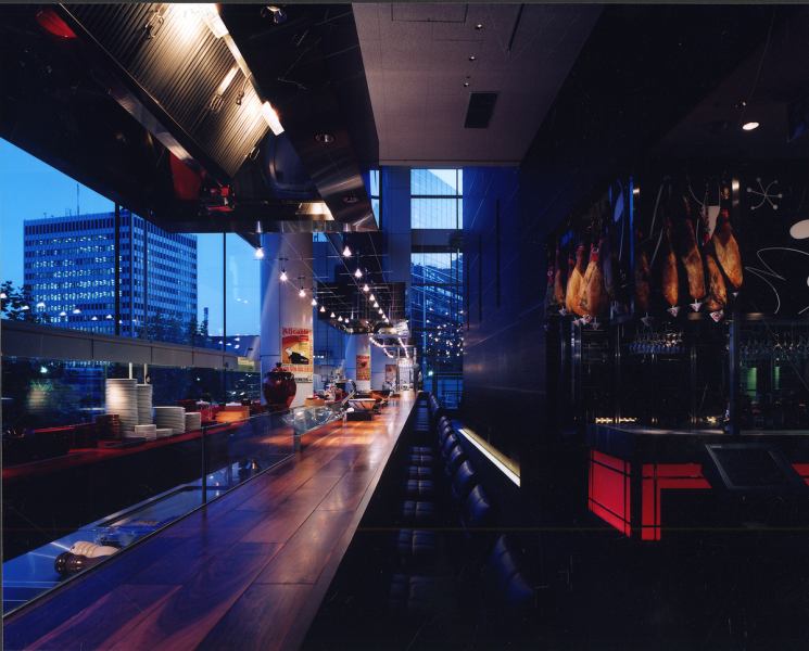 【天井高10mの開放的な店内】壮大な空間はまさに圧巻。丸の内を一望できる全面ガラス張りのロングカウンターはなんと30m。丸の内のきらめく夜景がロマンティック。丸ノ内デートや誕生日、記念日など特別な日にぴったりです。自慢の絶品スペイン料理とワインを楽しみながら、贅沢な時間をお過ごしください。