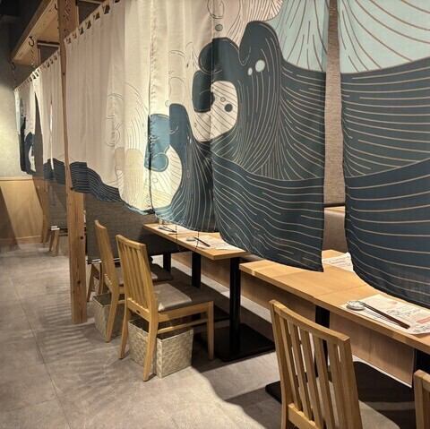 藍色の暖簾で仕切られたテーブル席は、周囲を気にせず会話を楽しめるプライベートな造りとなっています。女子会や少人数での飲み会など、親しい友人との食事にぴったりの環境です。清潔感のある内装と柔らかな光に包まれて、美味しい料理を囲みながら素敵なひとときをお楽しみいただける工夫が満載です。