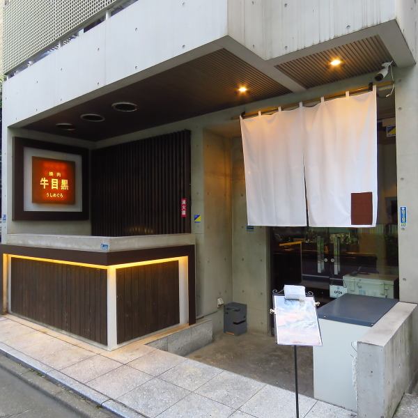 中目黒の通りにひっそりと佇む、洗練された大人の隠れ家。無機質なコンクリートと温かみのある木材が絶妙に調和したモダンな外観は、落ち着いた雰囲気を醸し出します。夜にはエントランスの暖かな光が上品に照らし、訪れる人々を優しく迎え入れます。この扉の向こうには、日常を忘れさせる上質な空間が広がります。