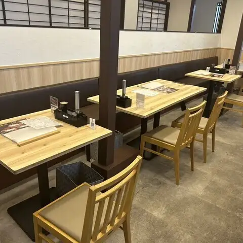 <p>明るい木目調のテーブルと椅子が規則正しく並ぶ清潔感あふれる店内です。壁面には和を感じさせる格子の造りが施されており心地よい雰囲気を演出します。席ごとにゆとりを持たせた配置となっておりご家族での普段使いやお仕事帰りのご利用まで様々な食事の場面で快適なお時間を過ごせます。</p>