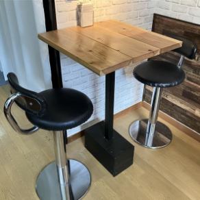 这张双人桌椅空间紧凑，宛如一个隐蔽的角落，非常适合约会或与好友聊天。一张时尚的黑色高脚椅，带有靠背，摆放在一张桌面为暖色调木质的桌子旁边。白色砖墙营造出柔和的氛围，为你们两人创造了一个特别的时刻。
