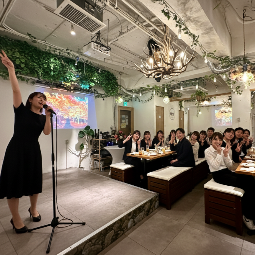 マイクを持ってスピーチする人物と着席する来場者。渋谷ガーデンパティオのステージ付きフロア