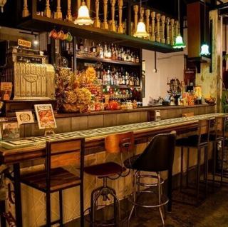【カウンター席：6席】色とりどりのボトルが並ぶ本格的なバーカウンターは、まるで海外のダイナーのような雰囲気。バーテンダーとの会話を楽しみながら、自家製ジンジャーエールを使ったハイボールやモヒートなど、種類豊富なドリンクを味わえます。お一人様は勿論、デートやサク飲みにもぴったりな居心地の良い特等席です