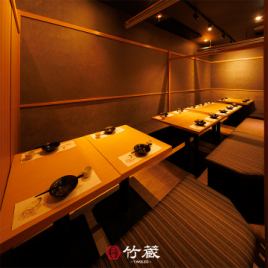 ［16～18名様：個室］木目のテーブルと深みのある照明が織り成す扉付き個室。横並びのレイアウトは、宴会のひとときを彩ります。ゆとりある座り心地と柔らかな空気感が、特別な時間をより豊かにします。