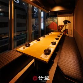［10～12名様：半個室］木の温もり感じる長テーブルと端正に設えた座席が、落着きを湛える和の半個室。窓から望む外の景色と、奥に掲げられた趣きある絵柄の仕切りが、非日常の情緒を添える特別席です。