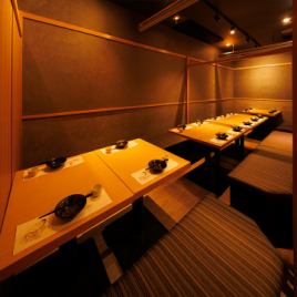 ［16～18名様：個室］木目のテーブルと深みのある照明が織り成す扉付き個室。横並びのレイアウトは、宴会のひとときを彩ります。ゆとりある座り心地と柔らかな空気感が、特別な時間をより豊かにします。