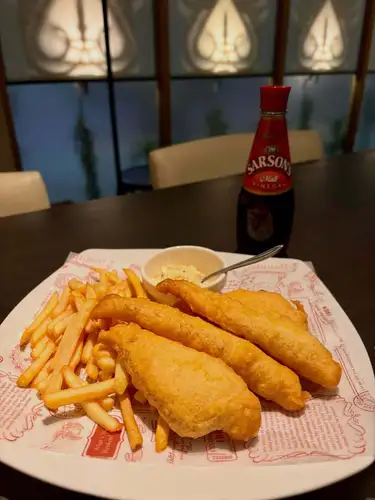 Fish & Chips

Fish and chips have been the undisputed No. 1 most popular menu item since the restaurant opened 🇬🇧 (apparently because there aren't many places that serve it 😅)

I recommend eating it British style, with plenty of malt vinegar.
How much is "plenty"? Well, enough to completely cover one slice on a small plate.
"You're putting that much on!?" you might be thinking 🫵 But you won't understand the deliciousness unless you pour this much on! (This is the owner's personal opinion)

We often have customers who become completely hooked on our products, so if you haven't tried them before or haven't used them in the past, give them a go next time you visit.
*Please be careful as the piping hot food served immediately after being prepared can easily cause choking.

The tartar sauce is included as a way to change the flavor or as an extra option for those who don't like vinegar.

For beer, Fuller's 🇬🇧 or Carlsberg 🇩🇰 would be a good match, and for cocktails, a gin and tonic would be nice, so please enjoy them together.