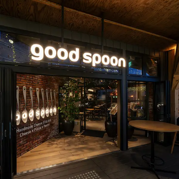 光るgoodspoonのロゴが目印。温もりあるエントランスの先で、焼き立ての窯焼きピザをお楽しみください。