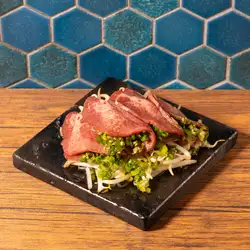 Grilled beef tongue with green onions and salt on a lava stone