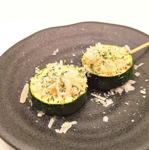 Charcoal-grilled zucchini skewers topped with Parmesan cheese