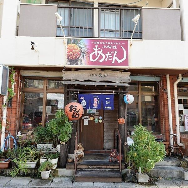 【創業37年・温かな名店】那覇市内から車で20分、屋冨祖通りからも徒歩圏内の好立地。看板メニューの「あだん」のロゴと赤提灯が、隠れ家のような安心感を演出します。一歩入れば、気取らない笑顔で迎えてくれるスタッフと、長年愛されてきた温かな空間が、心と体を解きほぐします。