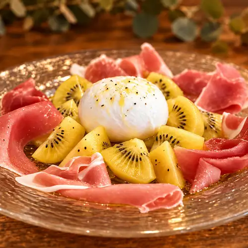 Burrata cheese and kiwi fruit caprese salad topped with prosciutto.