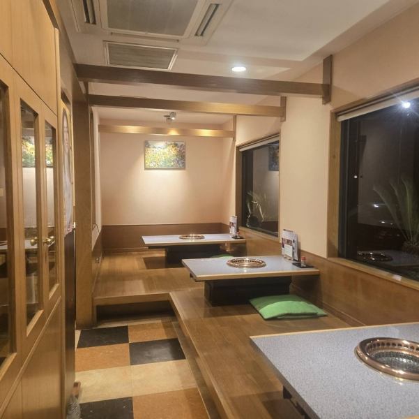 【木目調の優しい色合いに包まれた、ほっとする居心地の店内】大きく縁取られた窓からは、ネオンの明かりや移ろう季節の風景を見ることができ、ゆったりと寛ぎながら焼肉宴会をお楽しみいただくことができます。テーブル同士には程よい距離がございますので、気兼ねなくご飲食を満喫ください。