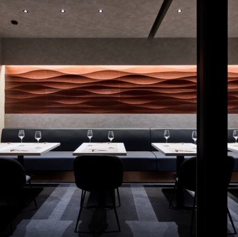 店内は昼と夜で異なる表情を見せ、ランチは自然光が心地よく、ディナーは間接照明が落ち着いた雰囲気を演出。一枚板の石カウンターや黒壁に映えるオレンジがかった照明など、上質な素材と設計の工夫が光ります。大人の時間をゆっくりと楽しめる空間です。