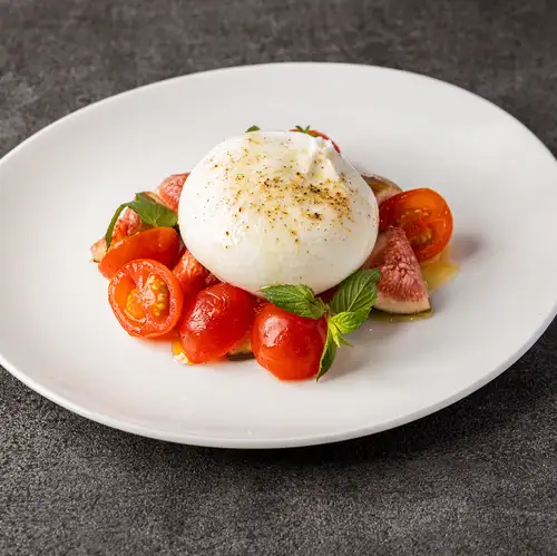 Caprese salad with burrata cheese, seasonal fruits, and tomatoes.