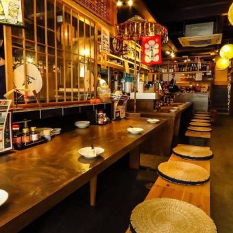 【カウンター席：16席】一人飲みからデートまで◎職人技を間近で満喫！目の前で繰り広げられる職人の手さばきを眺めながら、出来たてのお料理を楽しめる人気のカウンター席。全16席の広々とした造りで、お一人様のちょい飲みからデートまで幅広くご利用いただけます。鹿児島の味覚とお酒を心ゆくまでご堪能ください。