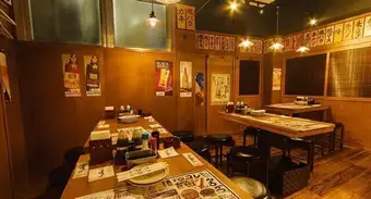 木目調の落ち着いたテーブル席は、世代を問わず皆様でゆったりとくつろいでいただける空間です。壁に並んだメニュー札が、居酒屋ならではの楽しい雰囲気を演出しております。お仕事帰りのお集まりやご家族での団らんなど、様々な場面に最適なお席です。牛脂で揚げた自慢の串かつや天ぷらを囲み、楽しいひと時をどうぞ！