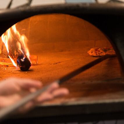 床やワインの木箱、薪などから木の温もりが溢れ、柔らかな照明が店内を包みます。ピッツァ職人が薪窯でピッツァを焼き上げる様子や、シェフが料理を仕上げる臨場感が楽しめるカウンター席もございます。ライブ感あふれるオープンキッチンを眺めながら、出来立ての絶品料理を五感でご堪能ください。