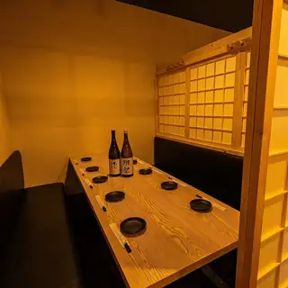 伝統的な格子戸のパーテーションが、どこか懐かしくもモダンな雰囲気を醸し出す半個室空間です。プライベート感がしっかりと確保された掘りごたつ席は、親しい仲間との語らいや、じっくりとお酒を味わいたい夜にぴったり。テーブルに佇むプレミアムな日本酒が、これから始まる特別な宴の時間を贅沢に彩ります。