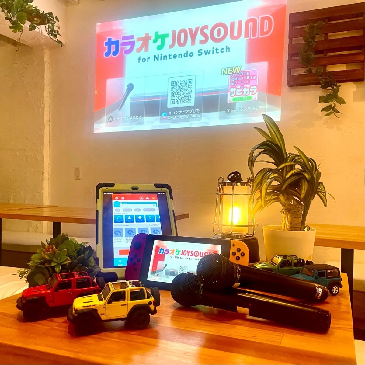 노래방 JOYSOUND의 화면을 벽에 투영해, 태블릿과 게임기, 마이크를 늘어놓은 테이블