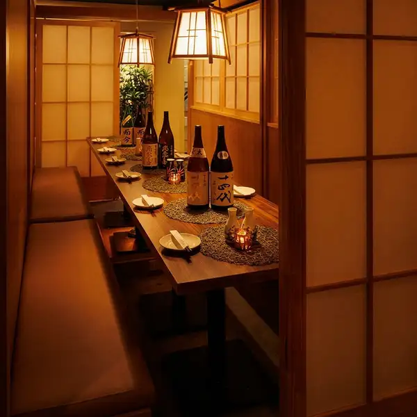 木の温もりに包まれた広々とした大空間。大人数でのご宴会や同窓会、会社終わりの飲み会に最適な、一体感のあるテーブル席をご用意しております。整然と並ぶ美しい一枚板のテーブルと温かい光を放つ竹籠風のランプが、和やかで心地よい宴の席を演出。貸切にも対応可能で、大人数でも皆様で快適にお過ごしいただけます。