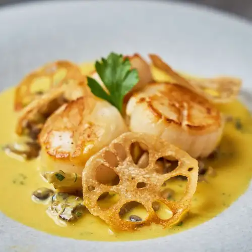 Pan-seared scallops with seasonal vegetables, autumn mushrooms, and saffron sauce.